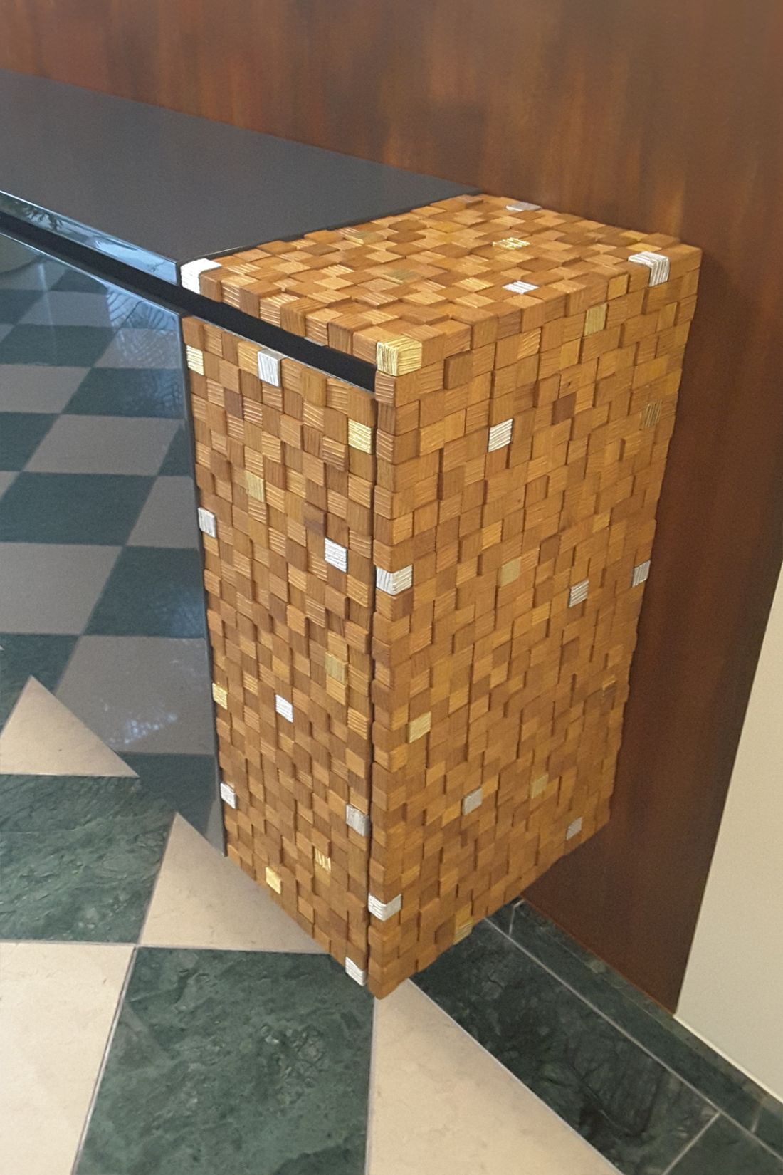 Wandkonsole mit Holz-Mosaik in Würfelform in Detailaufnahme mit anthrazit Hochglanz lackiertem Deckblatt, vor brauner Wand und Schachbrettboden aus Marmor.